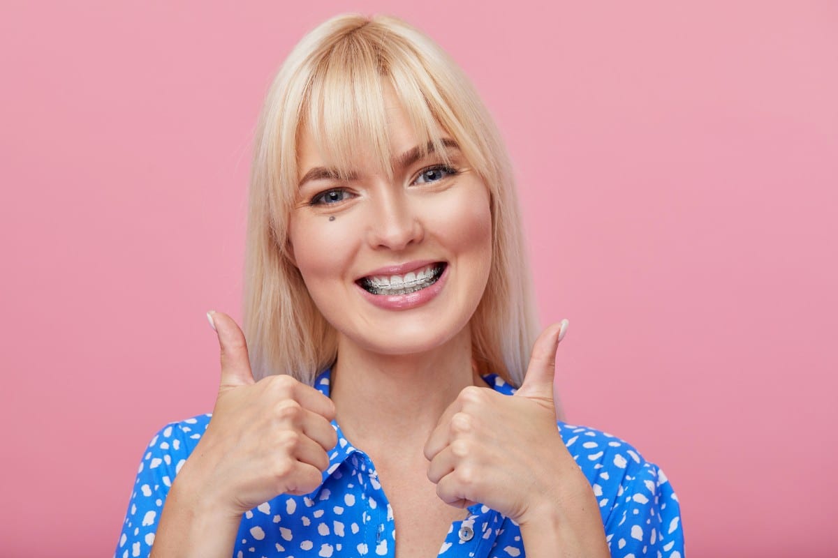 What You Need to Know About Nickel-free Braces Smiling woman with blonde hair giving thumbs up against pink background, dental professional portrait.