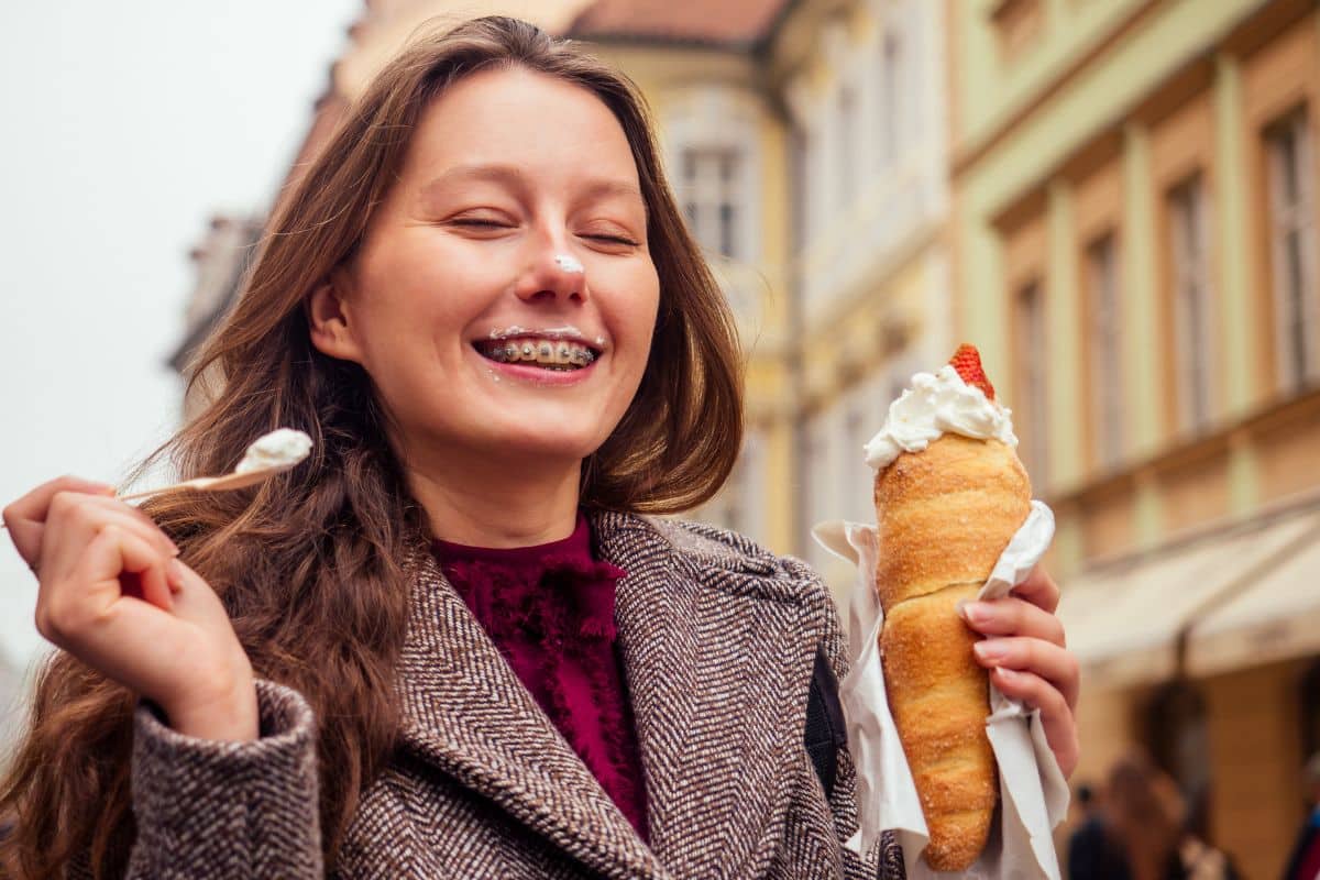 Taking Care of Your Braces During the Holidays Woman smiling while eating ice cream cone on a city street with historic buildings.