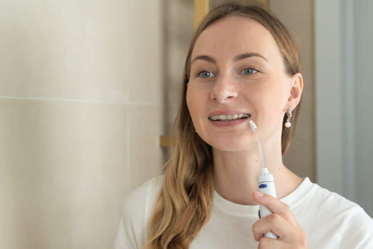 5 Cool New Gadgets for People with Braces Woman holding toothbrush smiling in bright dental office setting