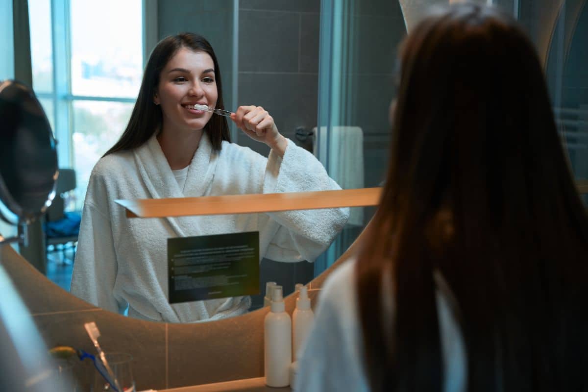Person brushing teeth A person brushing teeth in front of a bathroom mirror.