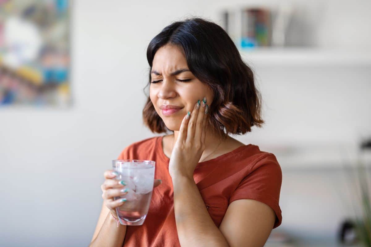 Emergency Dentist Woman experiencing tooth pain while holding a glass of ice water, showing signs of a possible dental emergency.