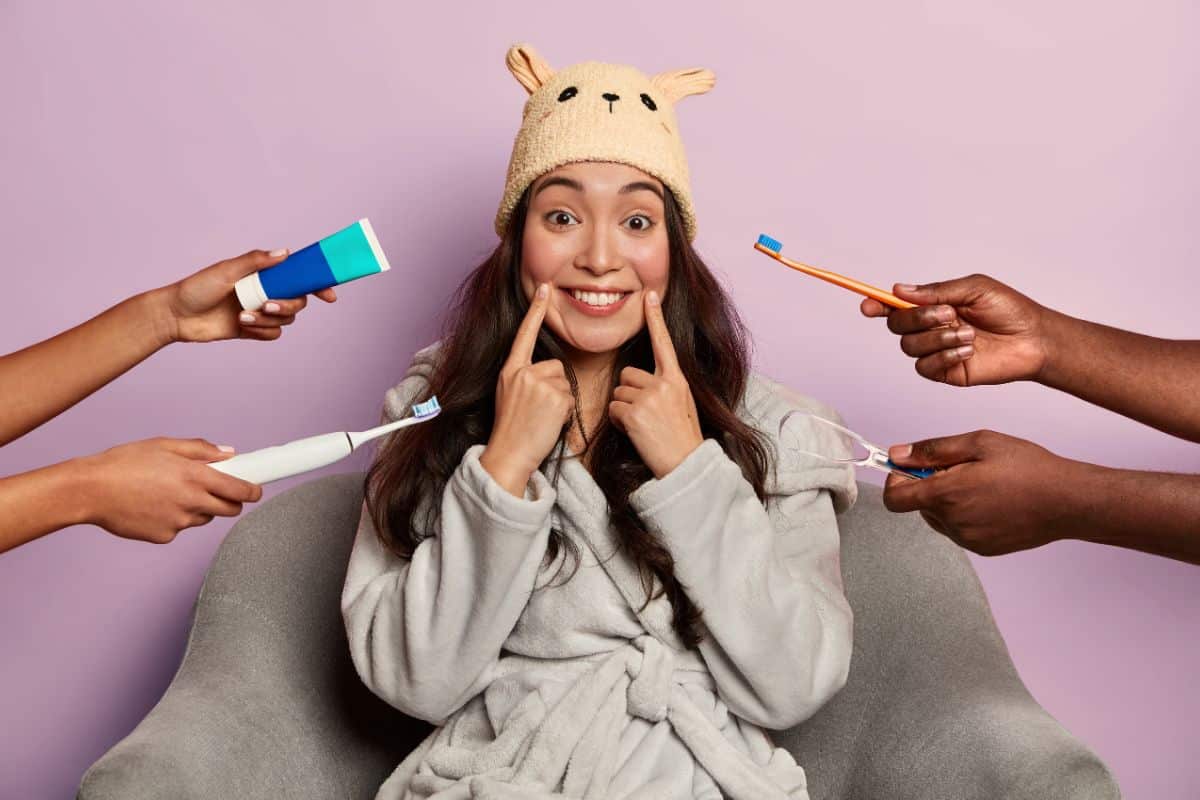 A cheerful woman pointing to her smile A cheerful woman pointing to her smile while surrounded by hands holding toothbrushes and toothpaste.