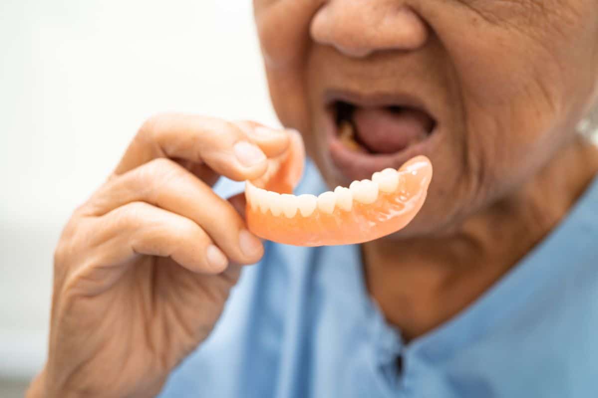 Dentures Older adult holding a lower denture while preparing to place it in their mouth.