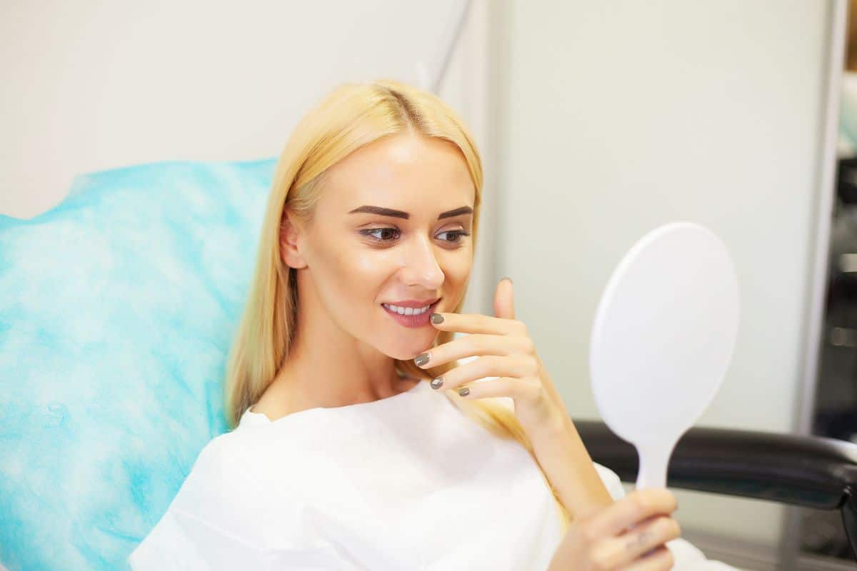 Cosmetic Dentistry Woman checking her smile in a hand mirror at a dental office.