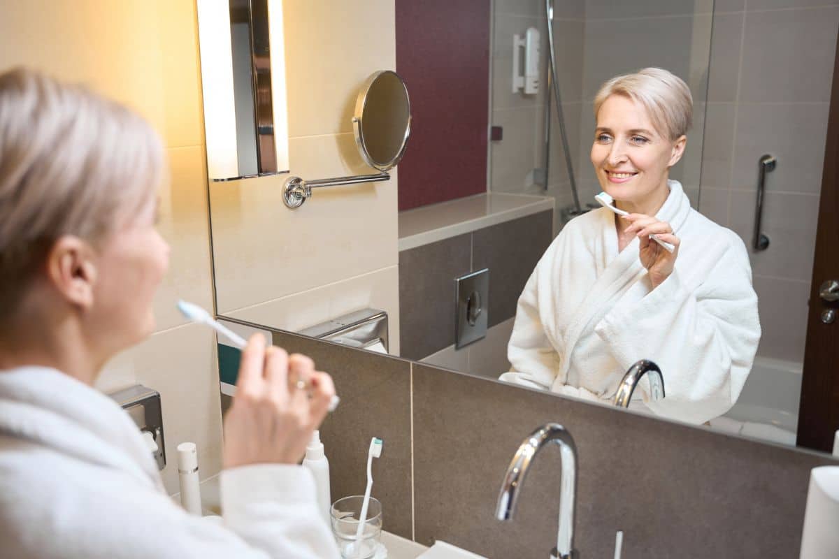 Woman brushing teeth properly in bathroom mirror.